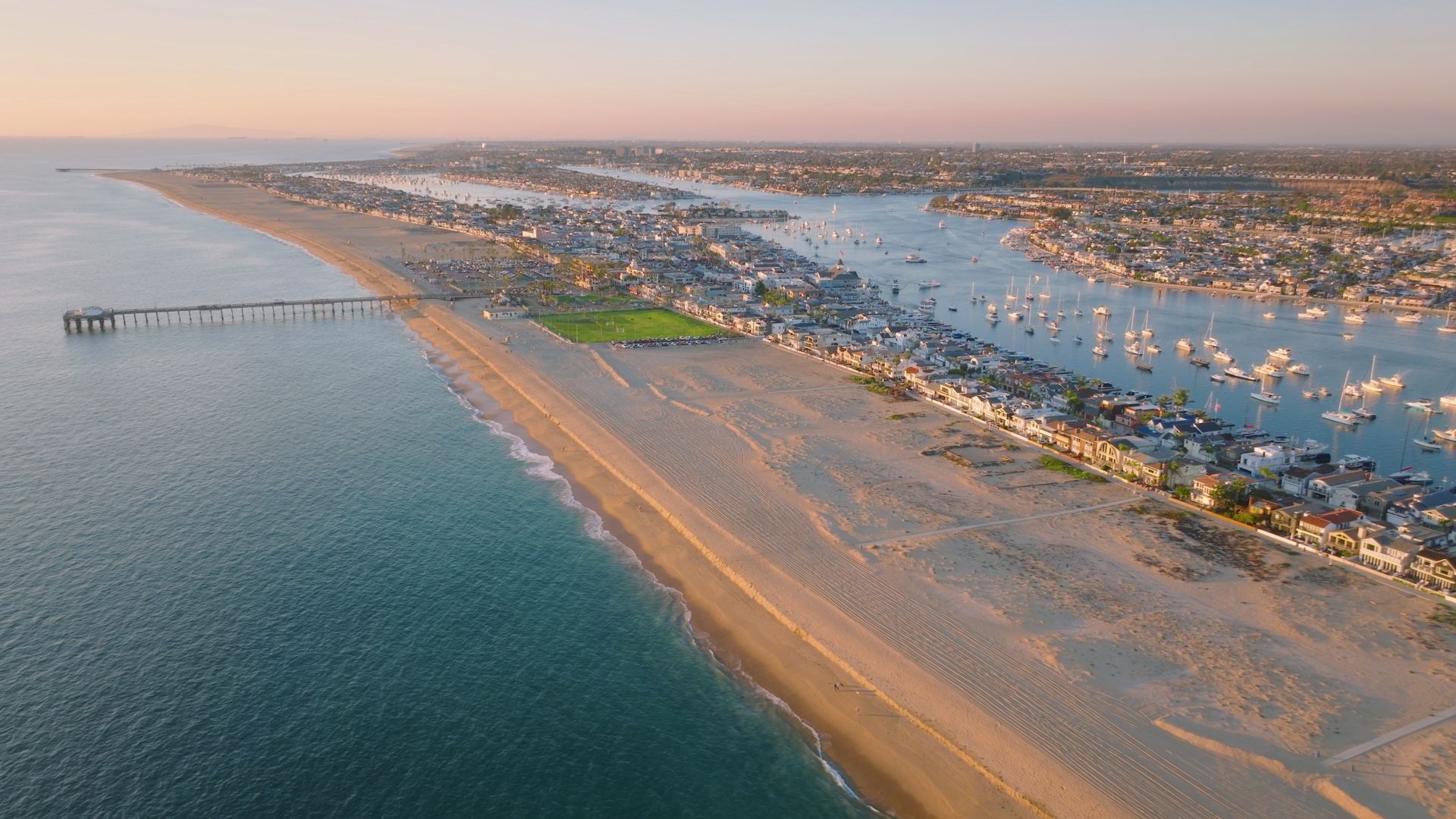 Aerial view of the Newport Beach Peninsula, pier, and harbor with boats moored along the channel